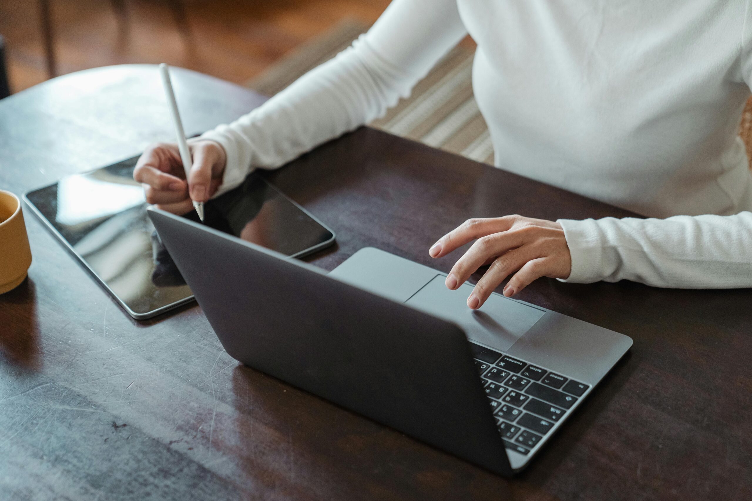 Focused businesswoman multitasking with a laptop and tablet in a modern office setting.