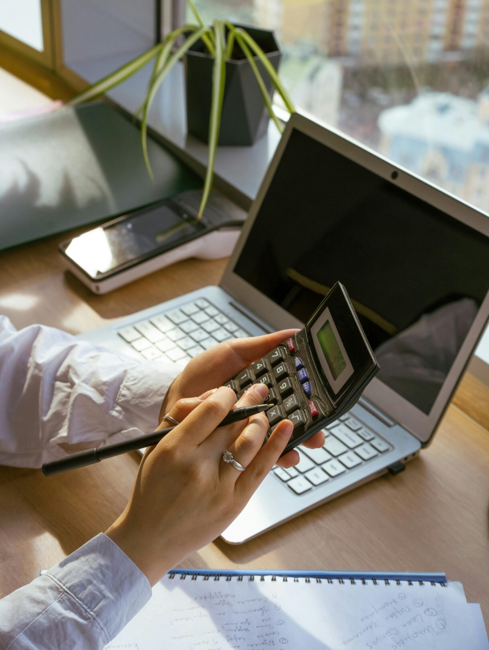Person calculating at desk with laptop and notebook. Ideal for business and finance themes.